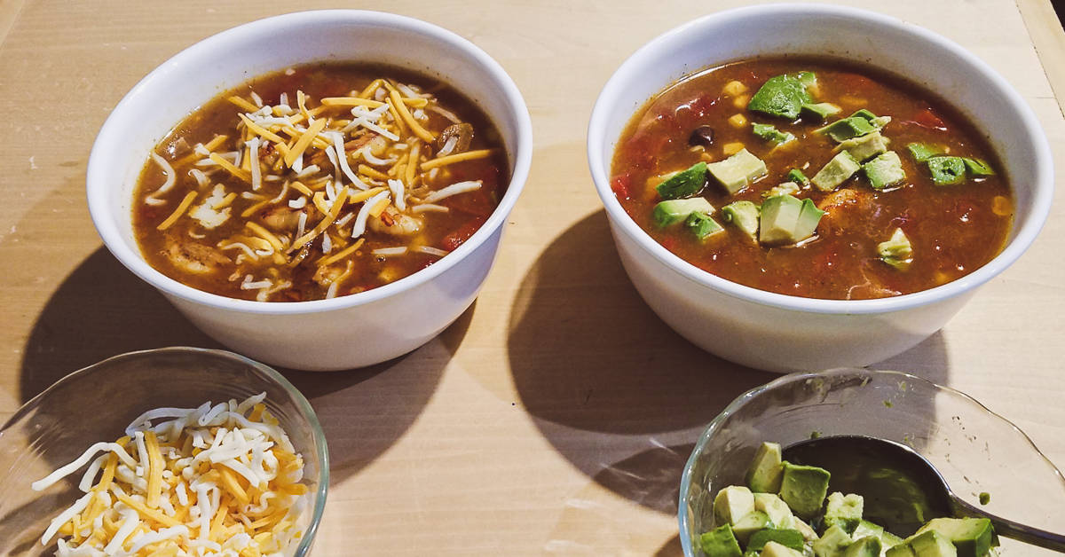 shrimp taco soup soup in large bowls with shredded cheese and chopped avocado