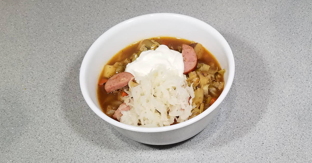 Kielbasa and Vegetable Soup in a bowl garnished with sour cream and sauerkraut