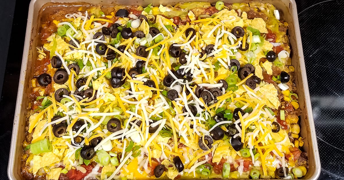 Layered Tex Mex Casserole garnished with green onions olives and tortilla chips